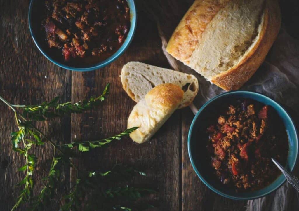 Two bowls of chili and bread on a wooden table.