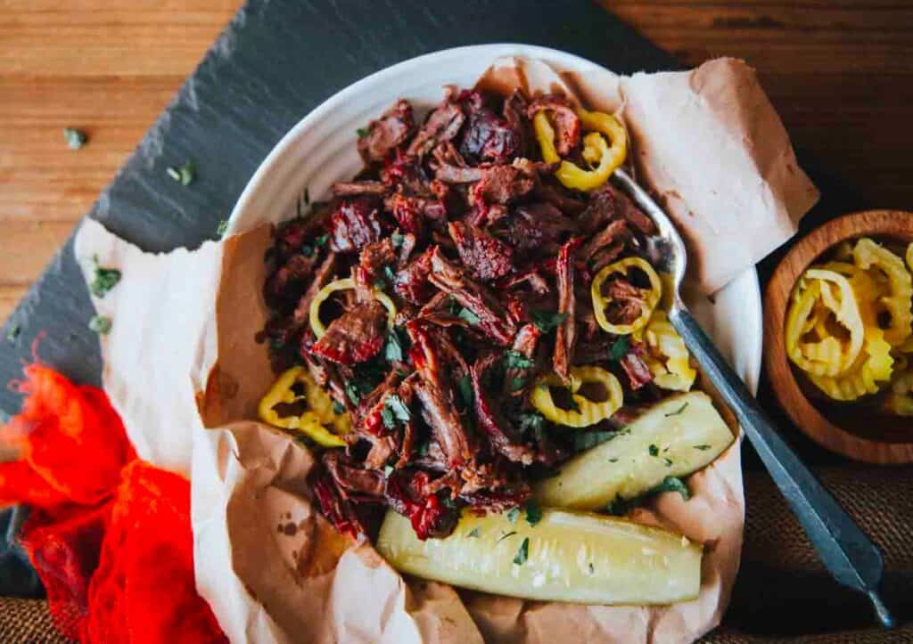 Bbq pulled beef on a plate with pickles.