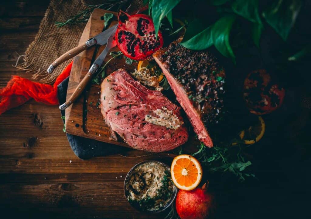 Smoked prime rib on a cutting board with oranges and herbs.