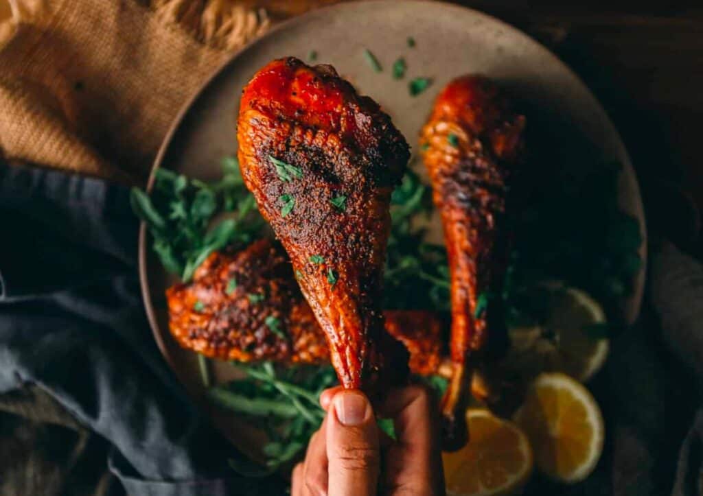 A hand holding a smoked turkey leg with lemons on it.