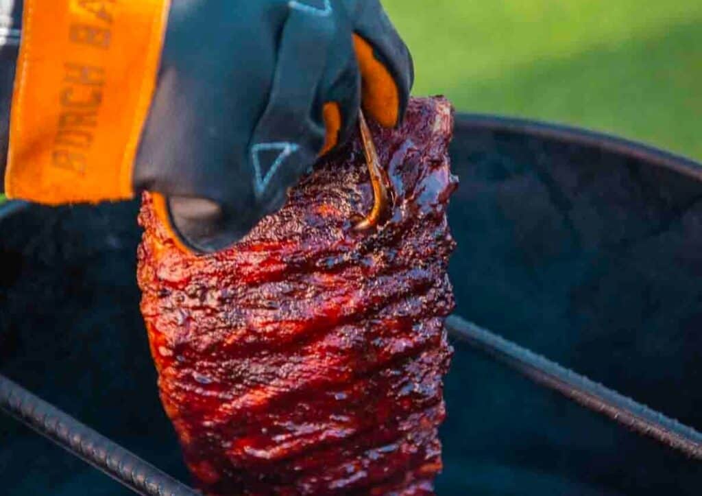 A person is holding a piece of ribs on a grill.