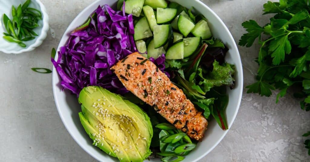 A mouthwatering bowl with the best salmon recipe featuring red cabbage and cucumbers.