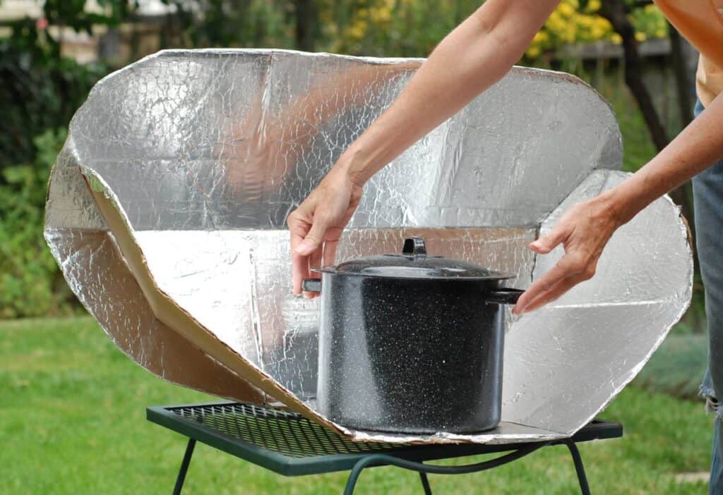 A woman putting a pot on top of a solar cooker.