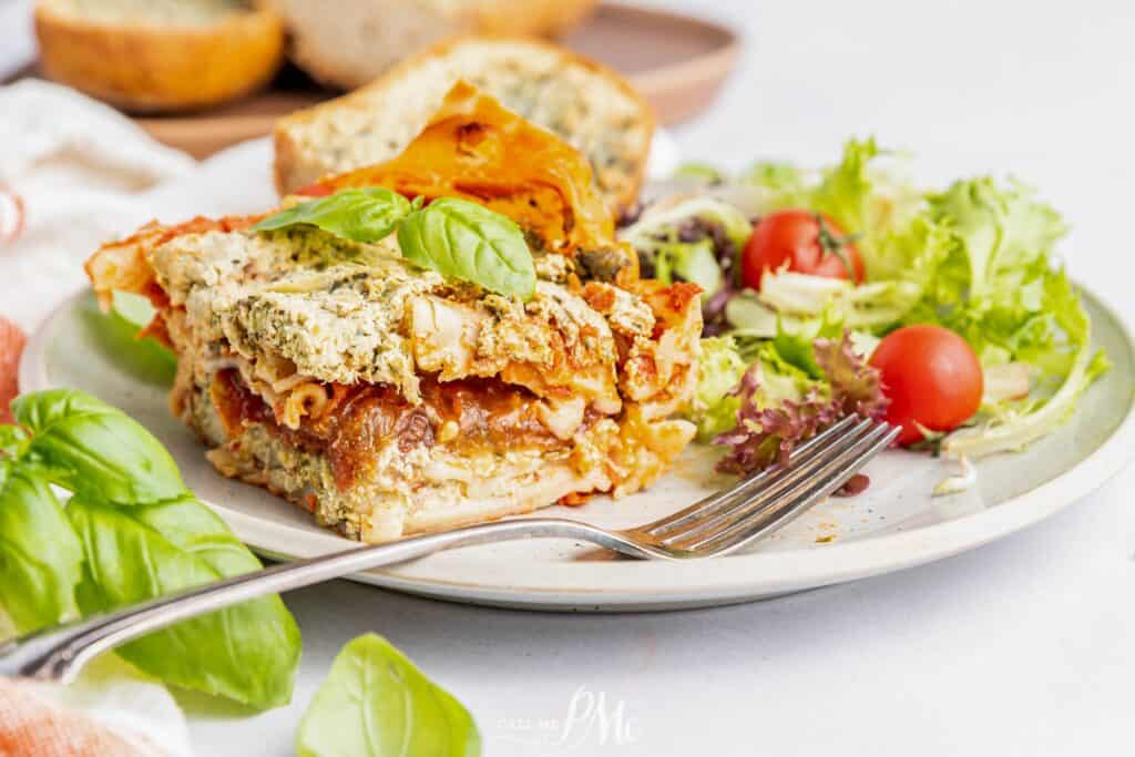 Veggie lasagna on a plate with a salad and fork.