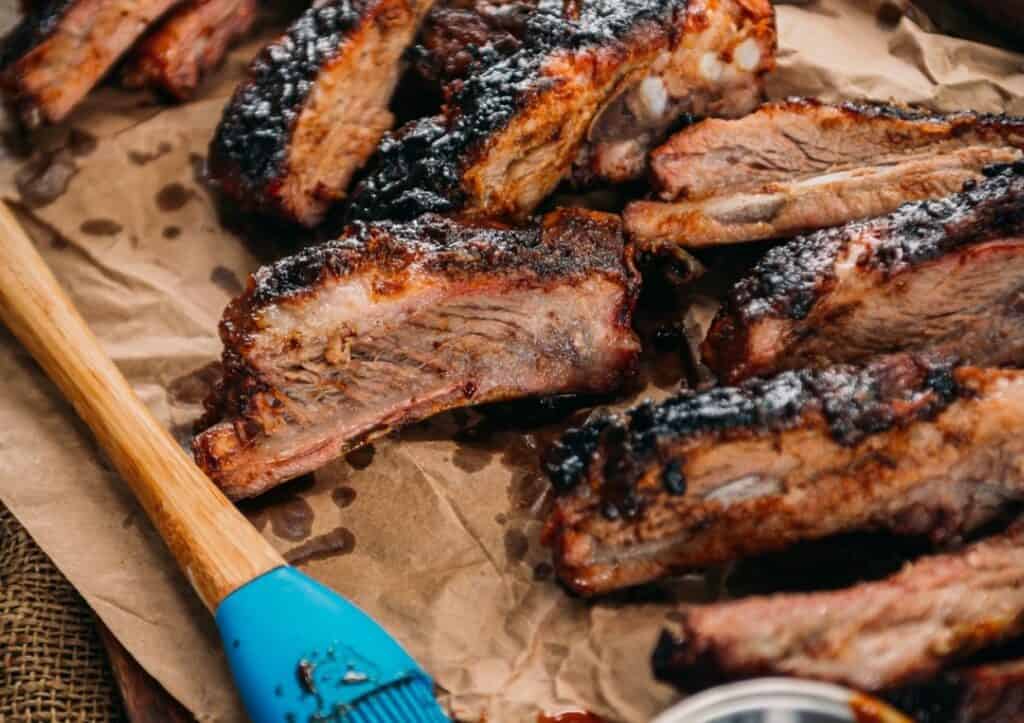 Bbq ribs on a wooden board with a blue spatula.