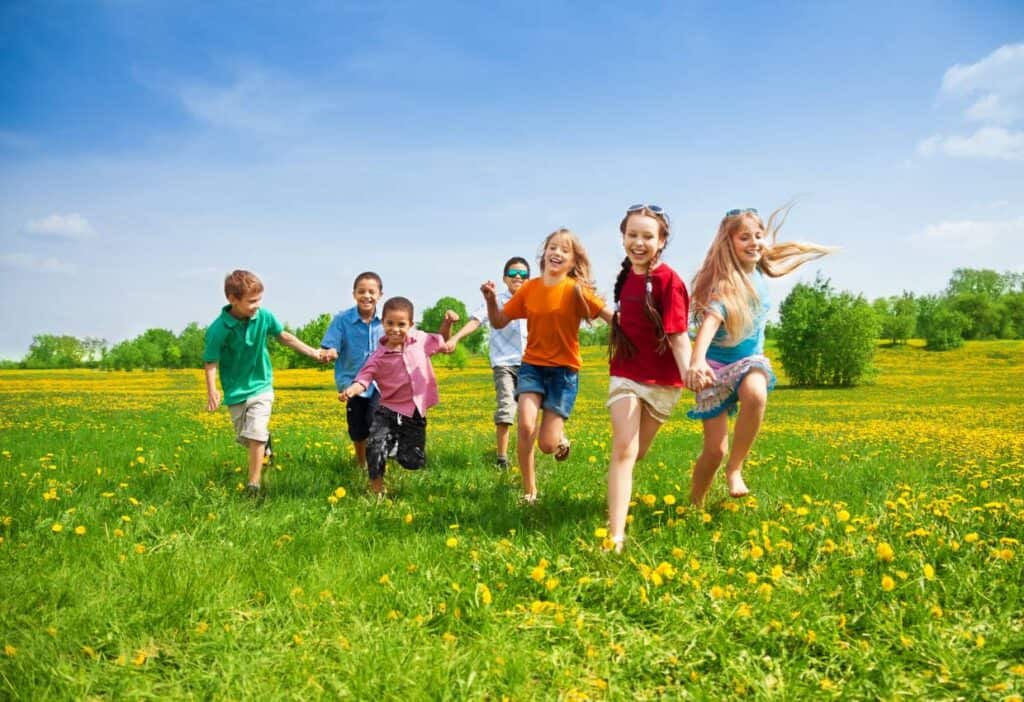 A group of children running in a field with dandelions.