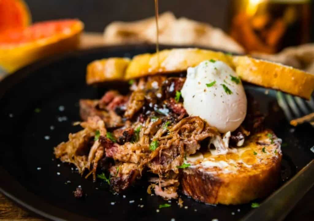 Bbq pulled pork sandwich with a poached egg on a black plate.