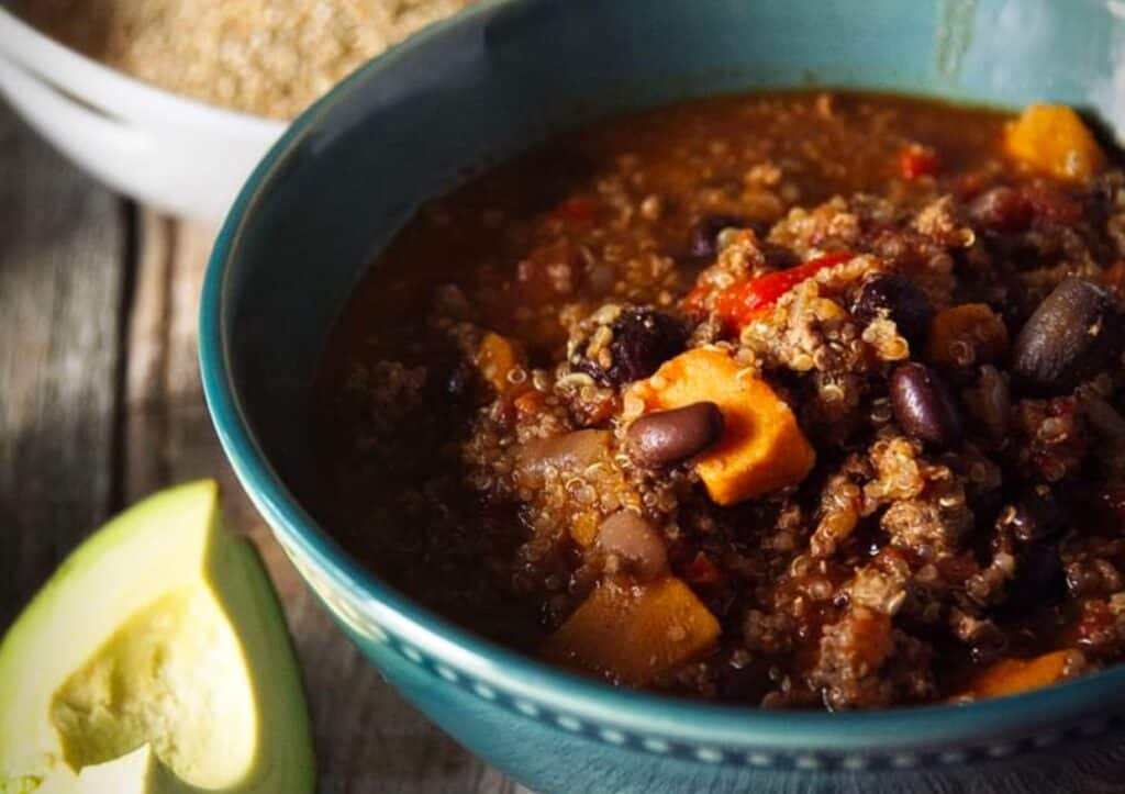 A bowl of chili with beans and avocado.
