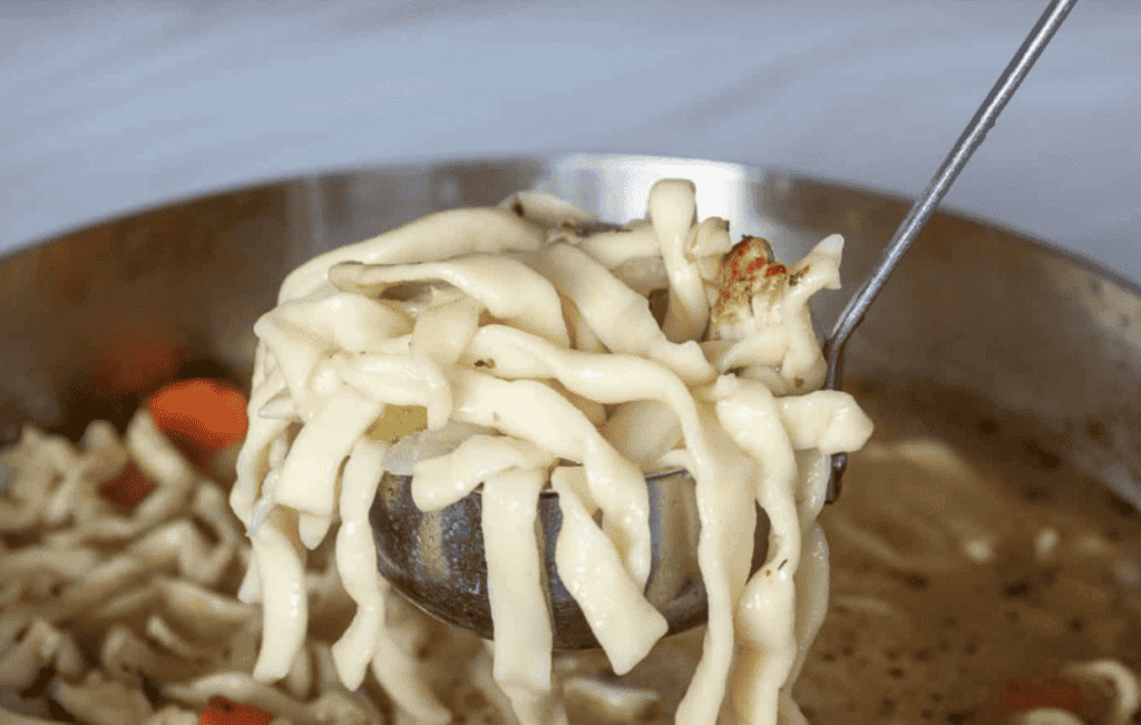 A spoonful of turkey noodle soup in a pan.