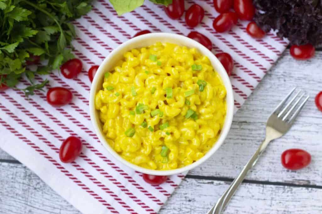 Mac and cheese food in a white bowl and on a white and white napkin. A fork lies next to the bowl of food.