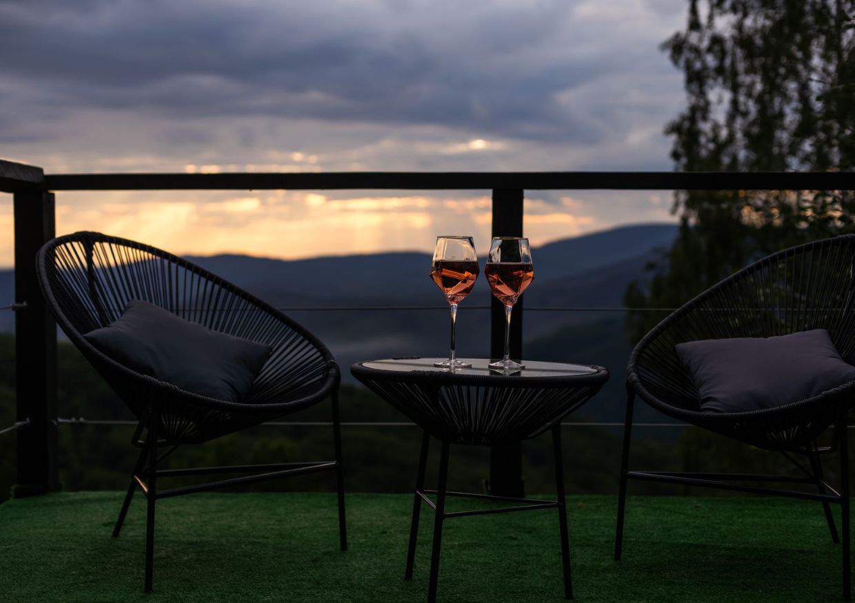 Two chairs with glasses of wine on a balcony overlooking the mountains.
