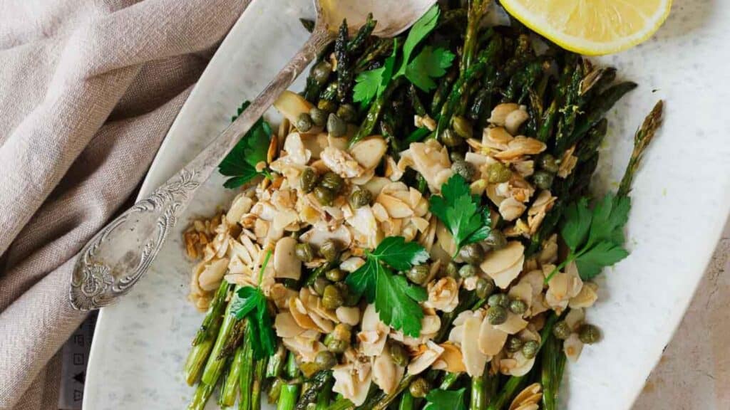 Asparagus with almonds and lemon wedges on a white plate.
