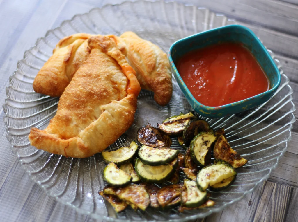 A plate with a calzone, zucchini and dipping sauce.
