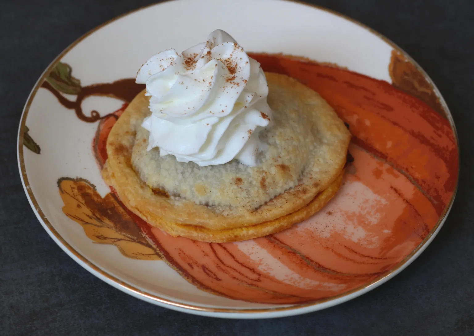 Pumpkin pie pop tart with whipped cream on top on a pumpkin plate.