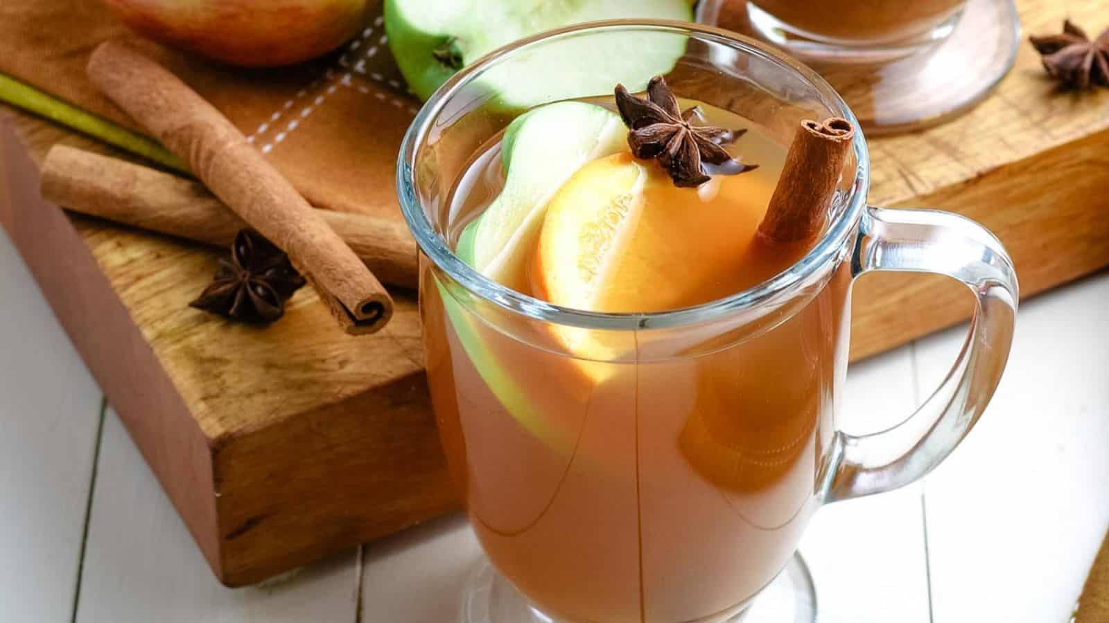 A cup of apple cider with cinnamon sticks and apples.