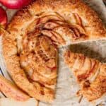 Overhead shot of an apple galette on parchment with fresh apples on the side.