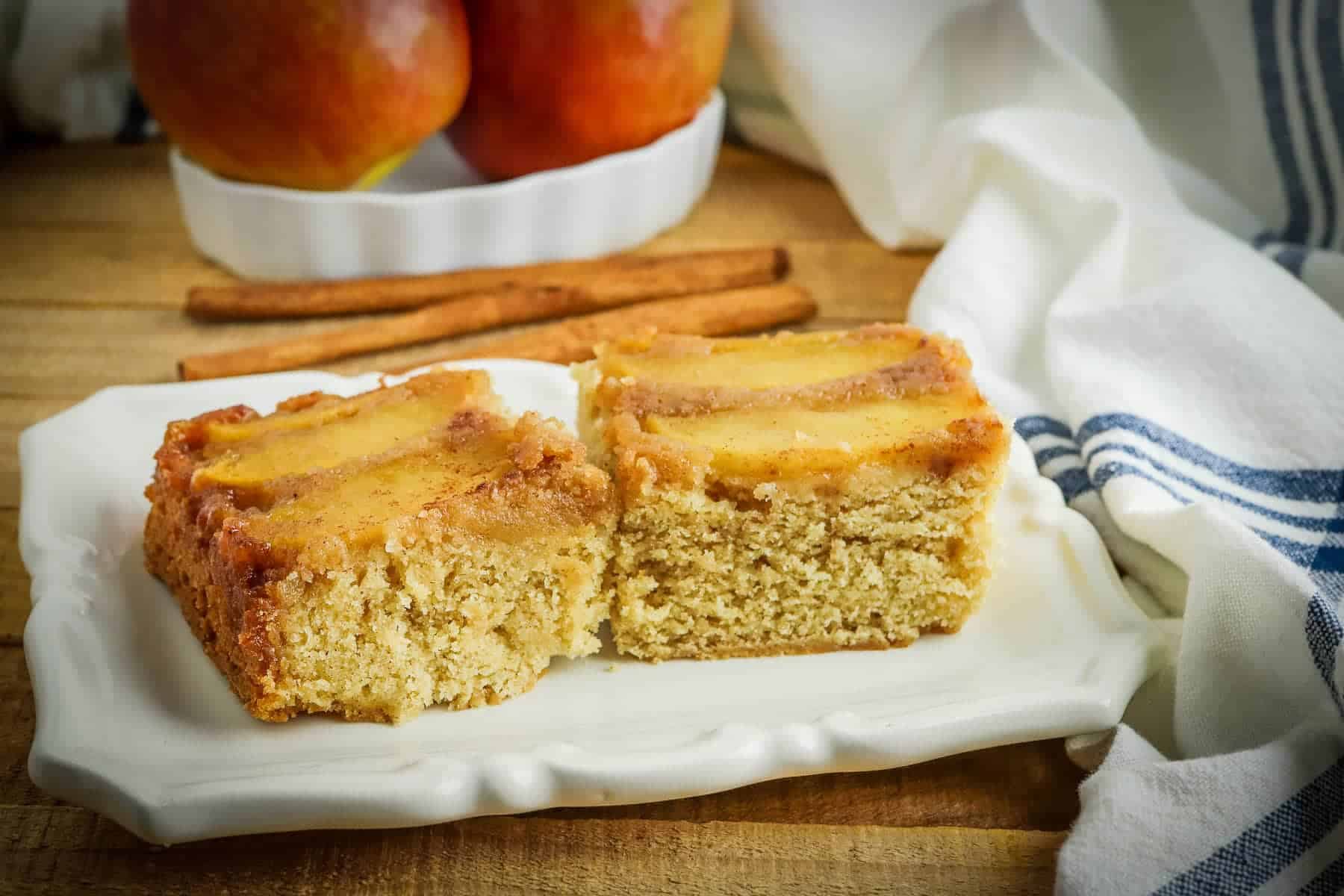A slice of apple cake on a plate with cinnamon sticks.