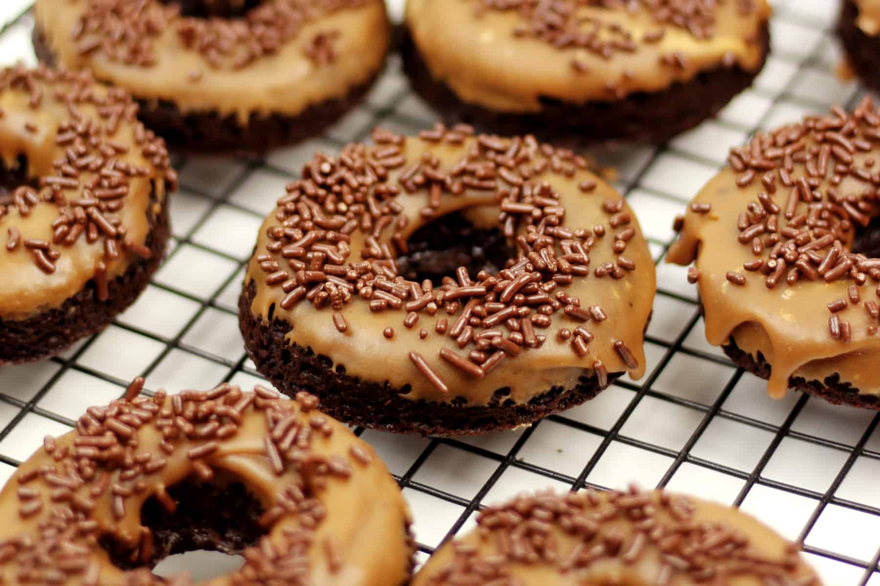 Donuts with chocolate icing and sprinkles on a cooling rack.