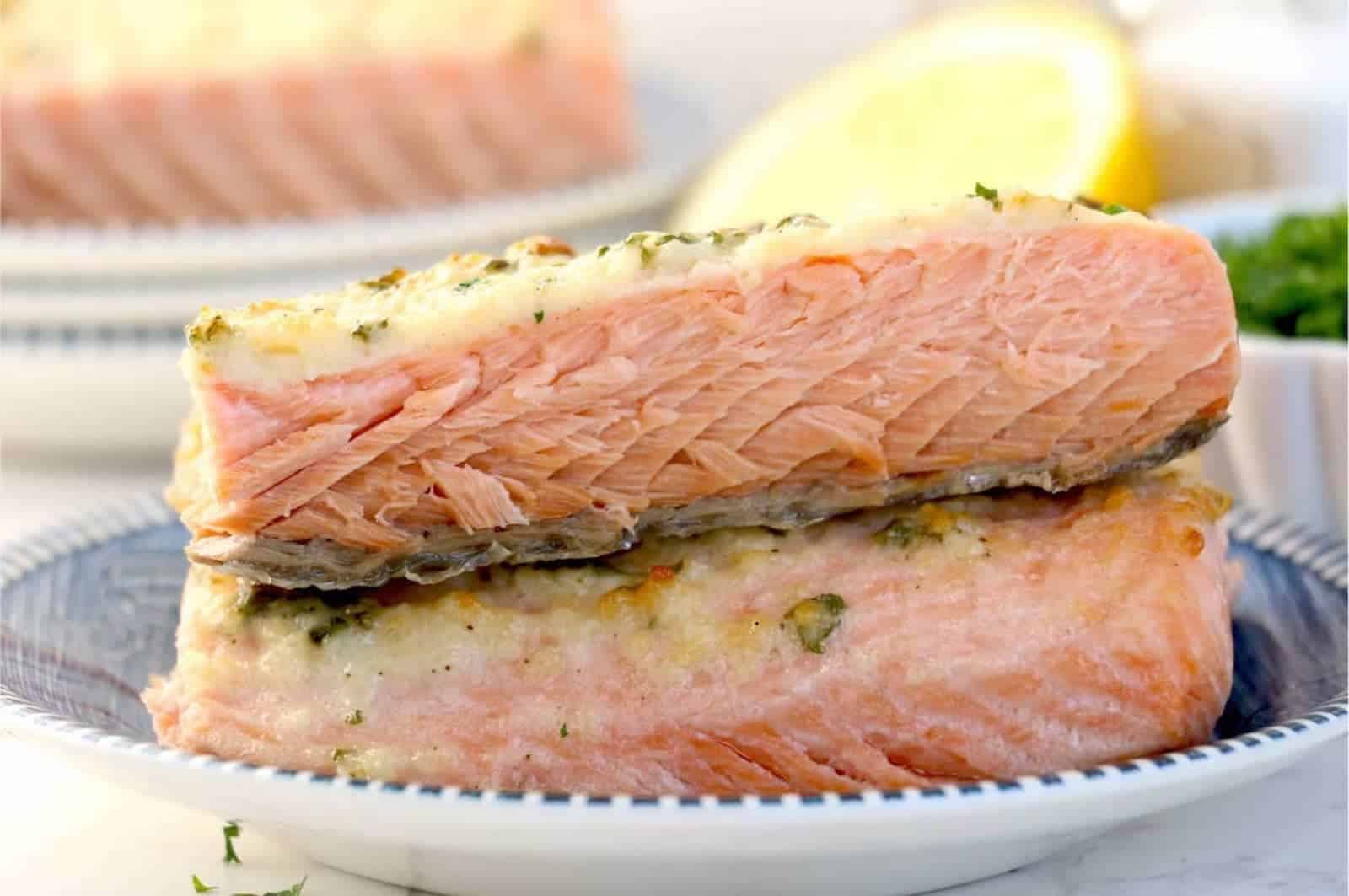 Salmon fillets stacked on a plate with lemons and herbs in the background.