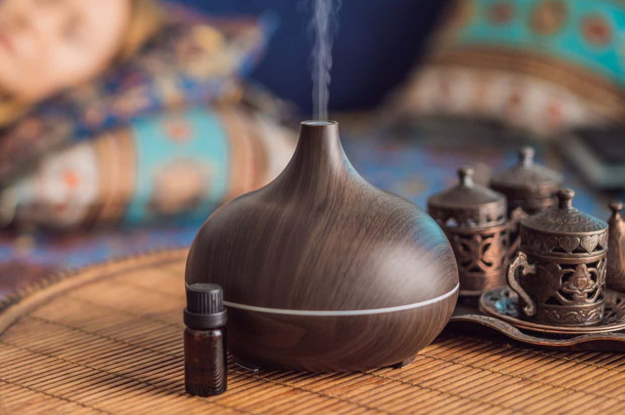 A wooden grain ultrasonic essential oil aroma diffuser on table with bottle of essential oil.