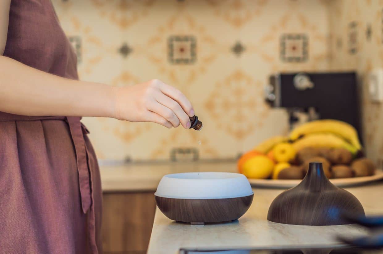 A woman is using an essential oil diffuser in the kitchen and adding oils.