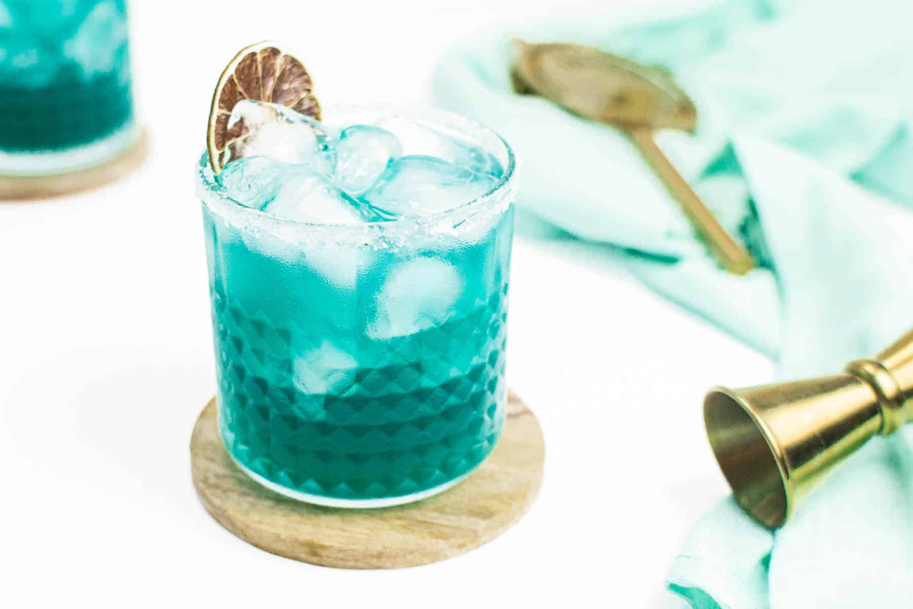 A blue drink with ice and a gold spoon.