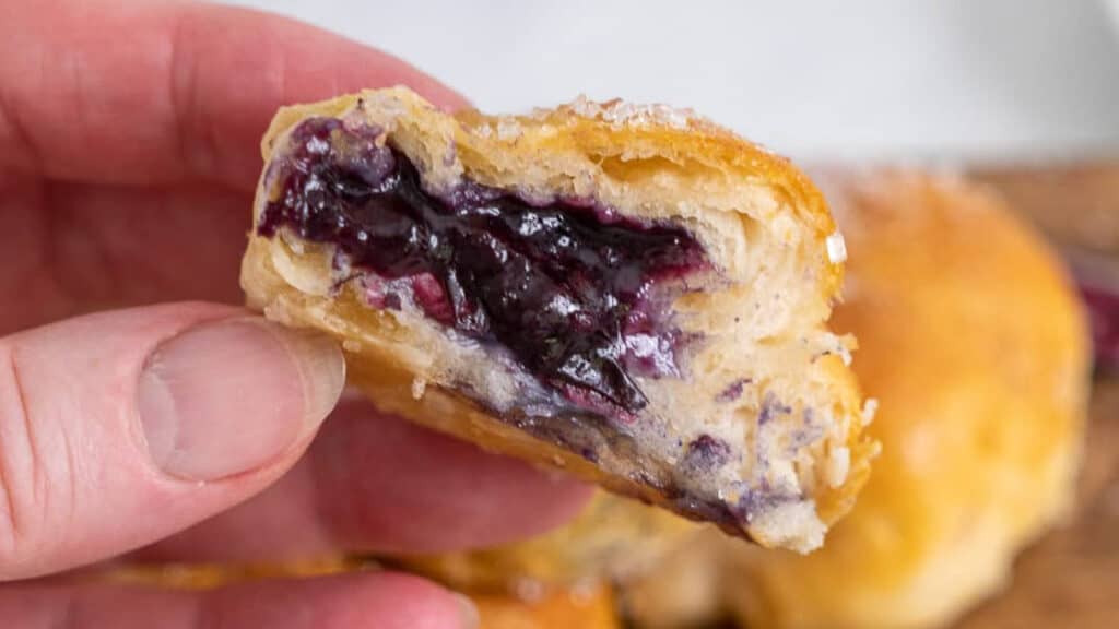 A person holding a pastry with blueberry filling.