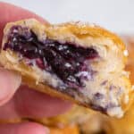 A person holding a pastry with blueberry filling.