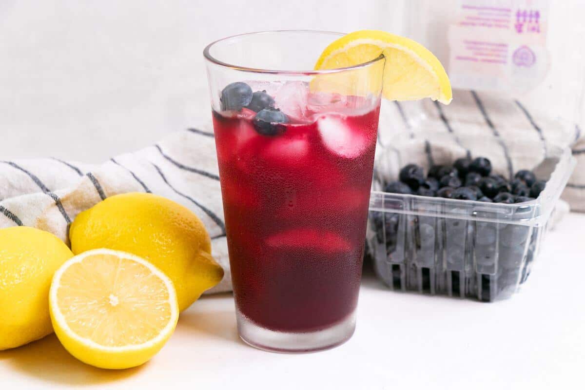 A glass of blueberry vodka lemonade with lemons and blueberries.