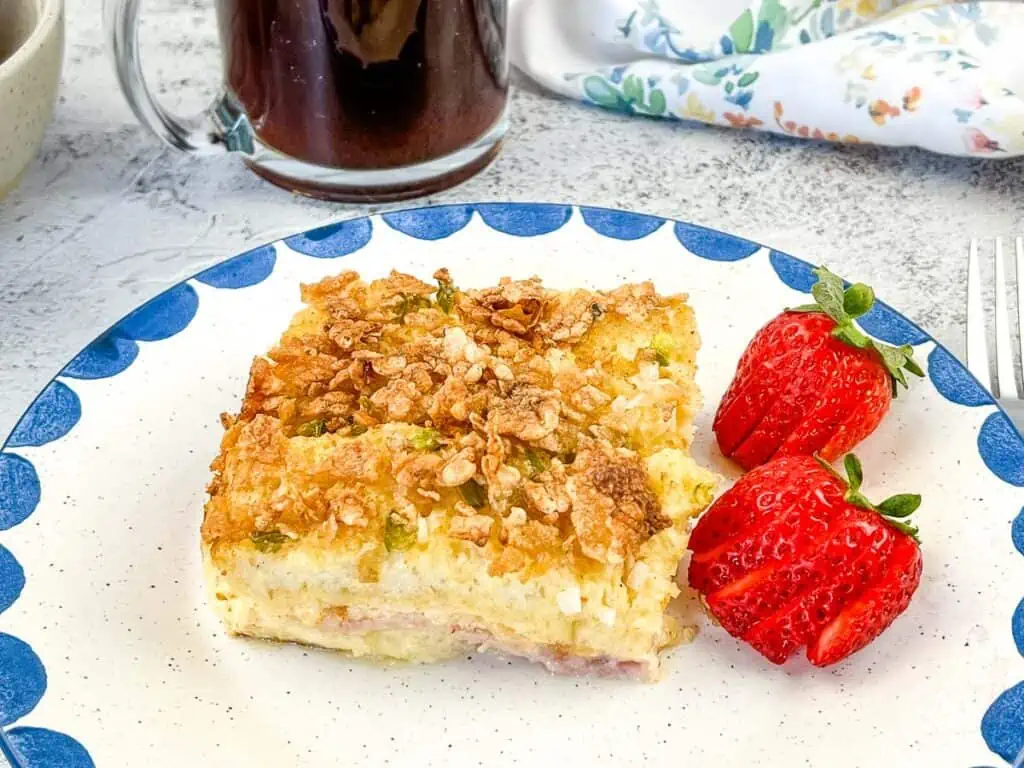 A piece of breakfast casserole on a plate next to a cup of coffee.