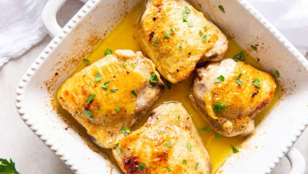 Chicken thighs in a white dish with lemon and parsley.