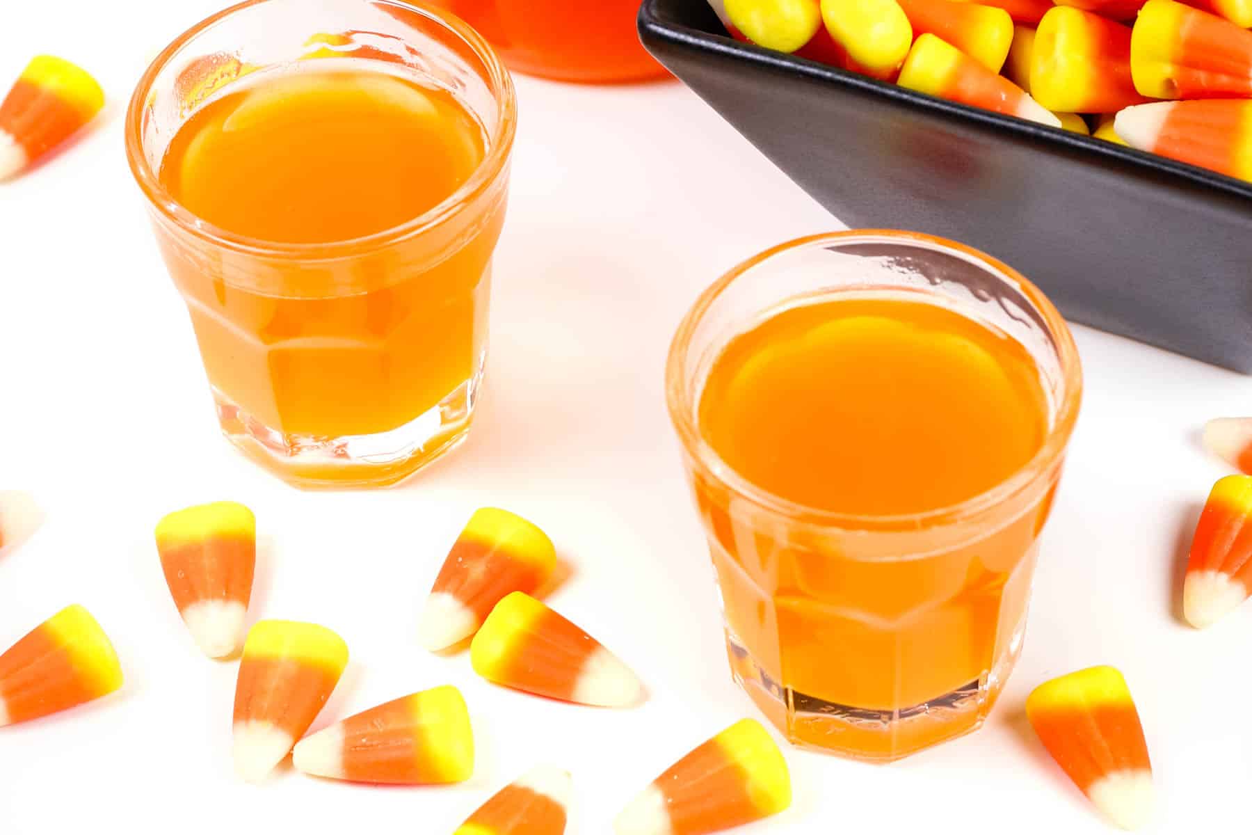 Two shots of candy corn vodka next to candy corn.