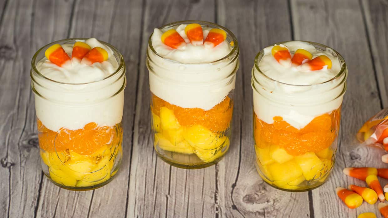 Three mason jars with candy corn fruit and yogurt parfait in them.