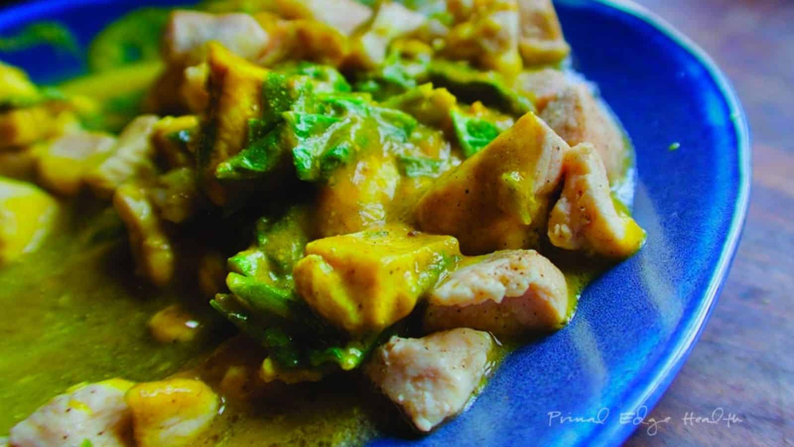 A blue plate with chicken and pumpkin in a curry sauce.