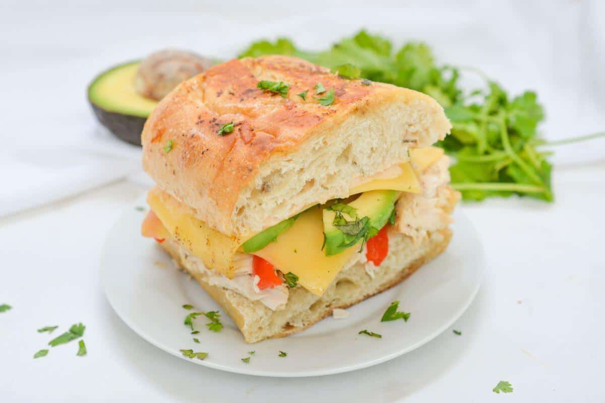 A sandwich with avocado, chicken and cheese on a plate.