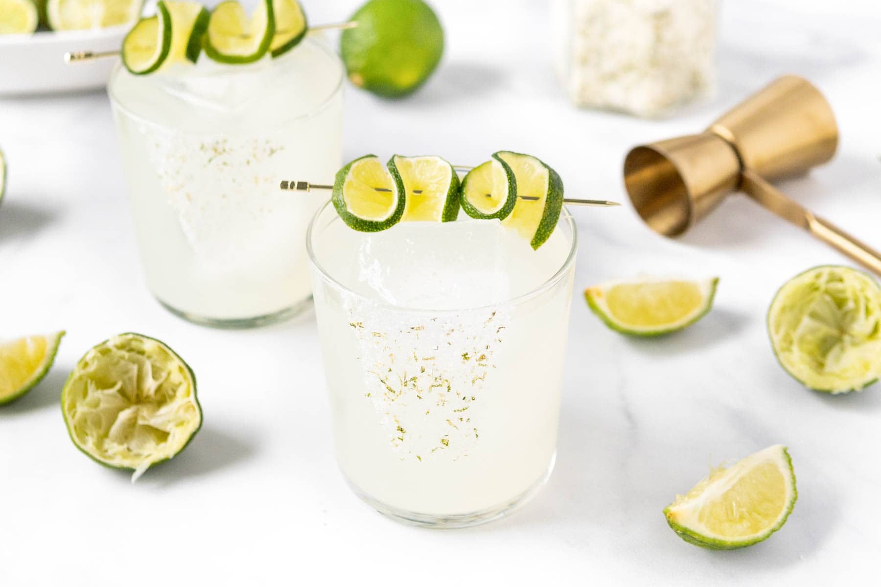 Two margarita glasses with limes and garnishes.