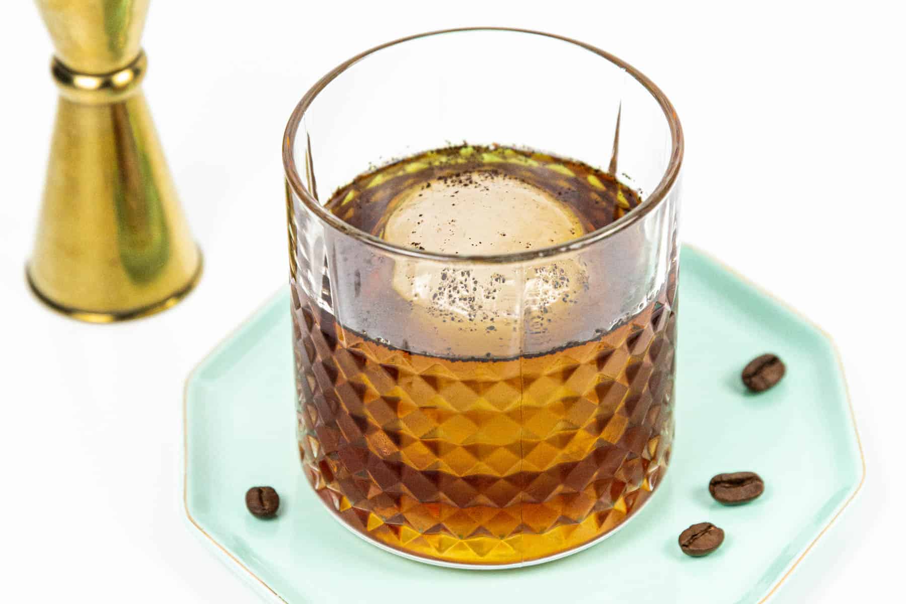 A glass of coffee cocktail with ice and coffee beans on a plate.