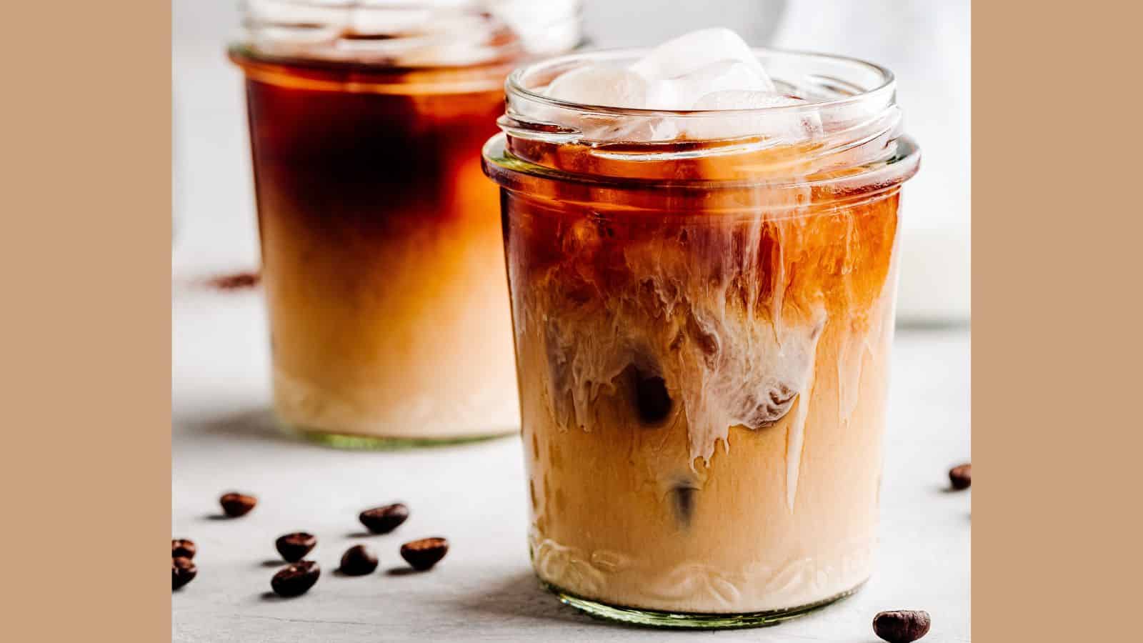Two glasses of iced cold brew coffee with cream and coffee beans.
