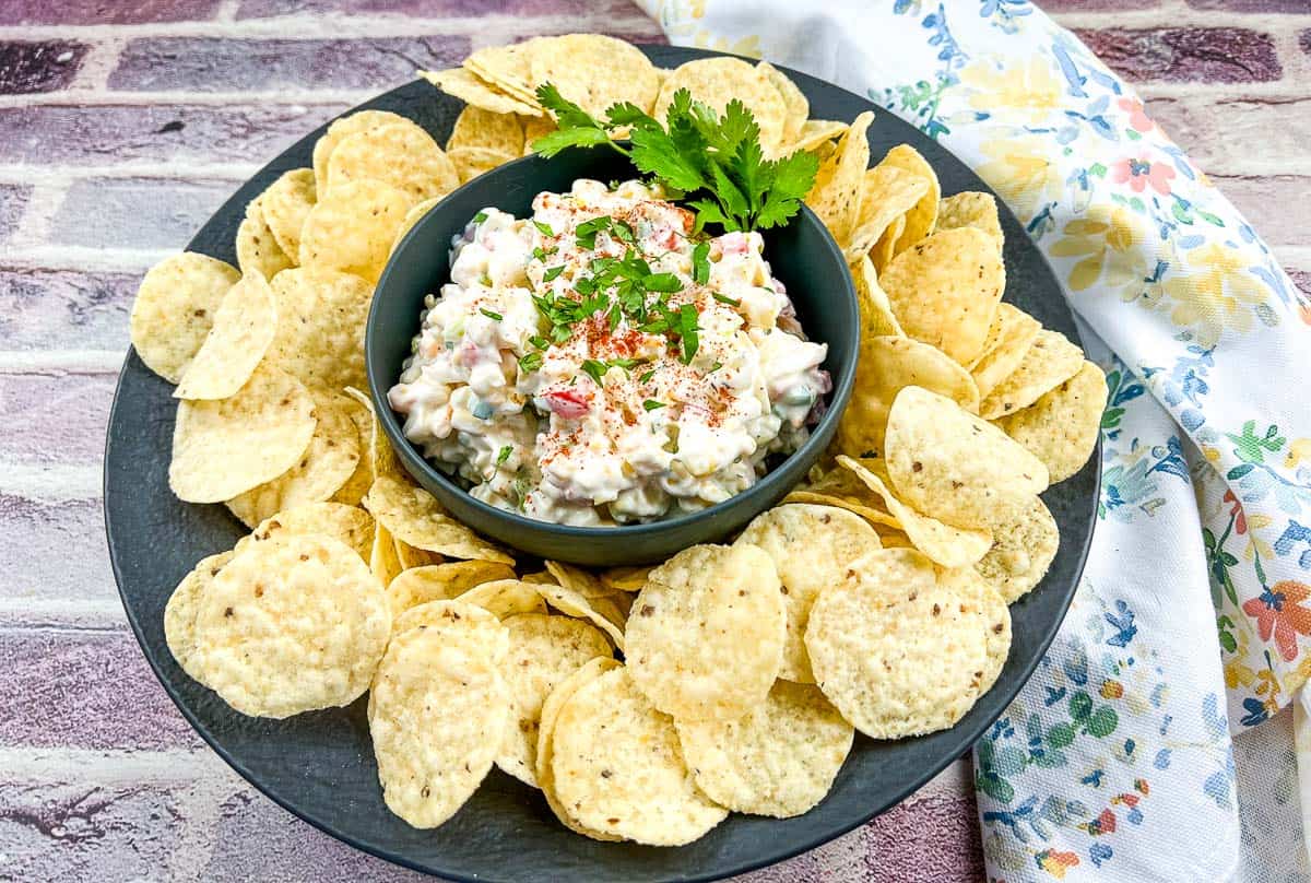 A bowl of Chilled Corn Dip with chips on a black plate.