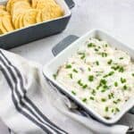 A bowl of cold crab dip with crackers and chives.