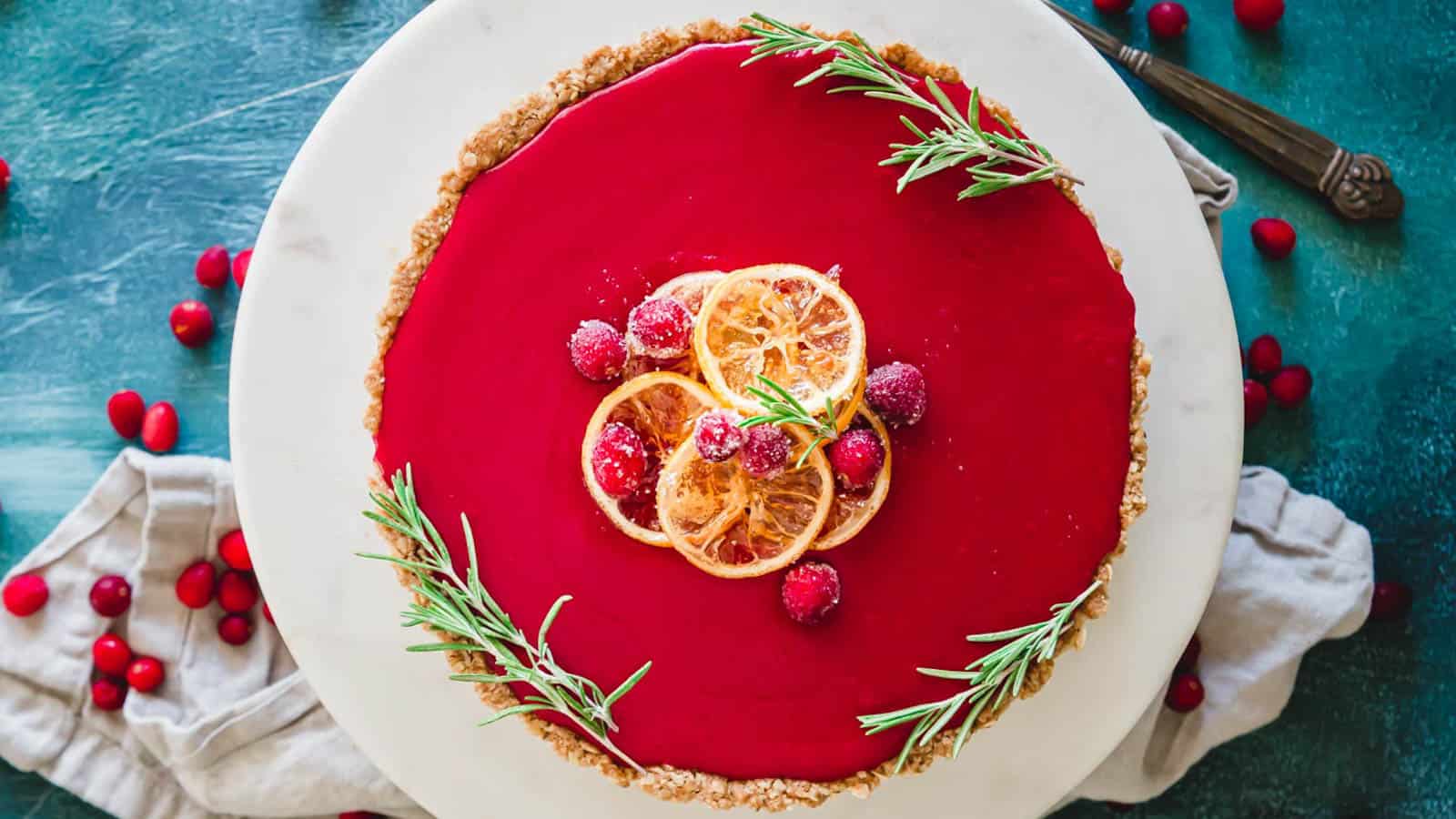 A cranberry curd tart on a plate with rosemary sprigs and candied lemon slices.