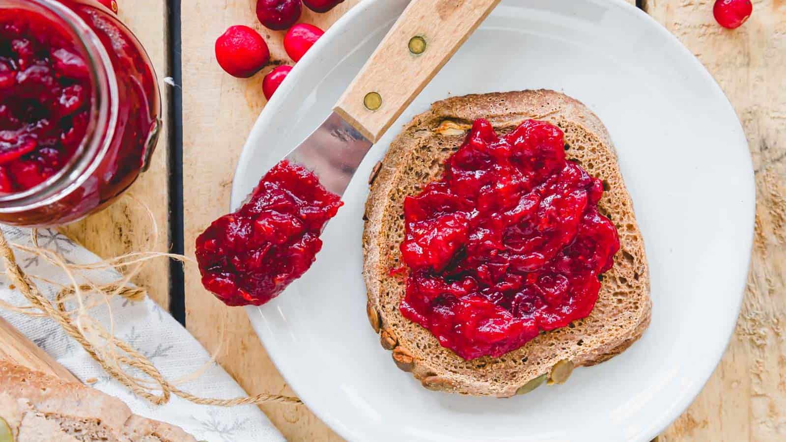 Cranberry ginger jam on bread with a wooden spoon.