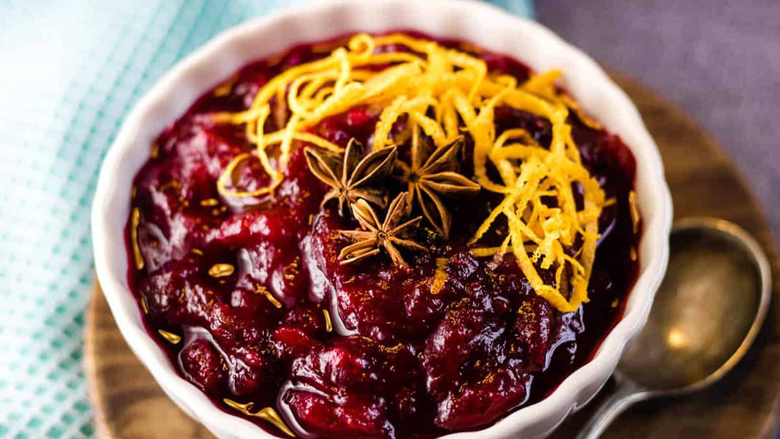 Cranberry sauce in a white bowl garnished with orange zest and star anise pods.
