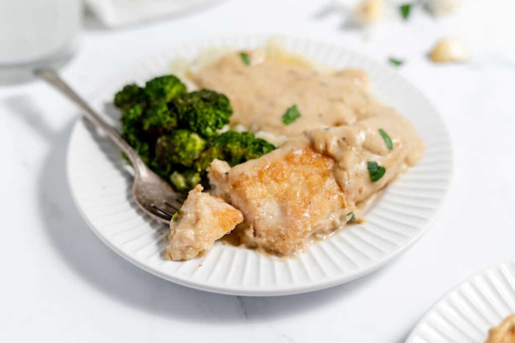 Creamy garlic chicken on a white plate with vegetables and mashed potatoes. 