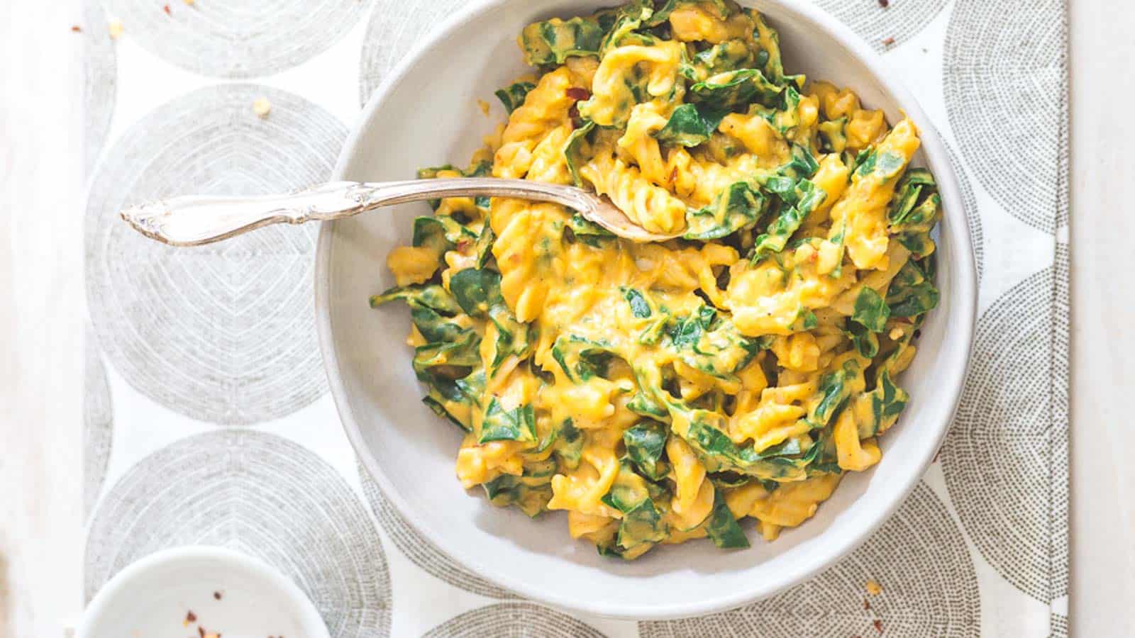 Creamy pumpkin pasta with garlic and tuscan kale in a bowl with a spoon.