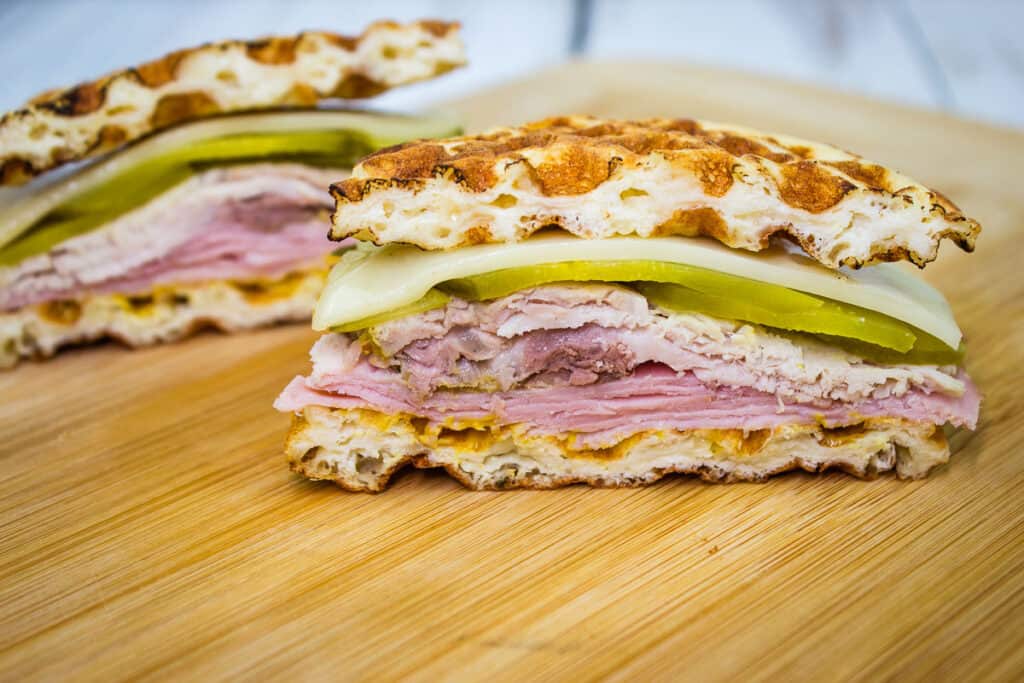 A sandwich with ham and pickles on a wooden cutting board.