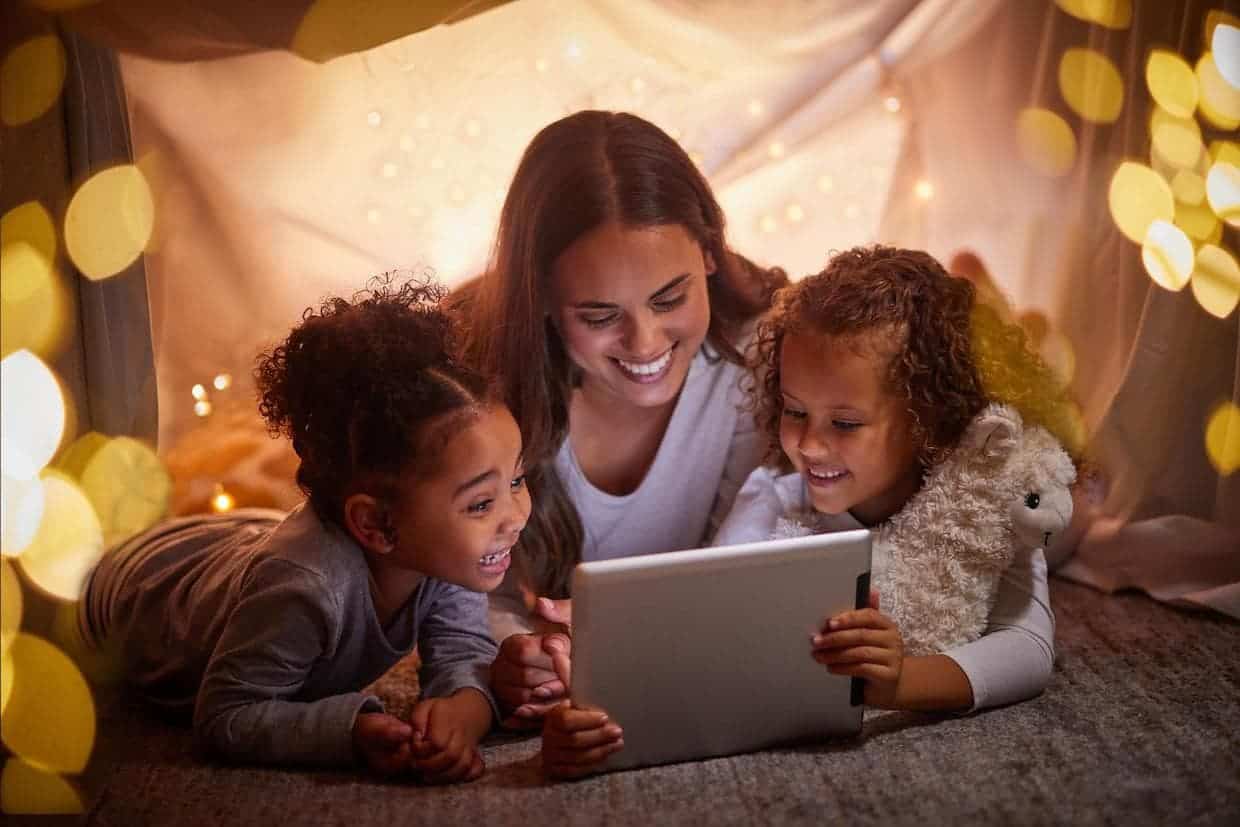 Mother with two girls watching family camping movies on a tablet in a tent. 