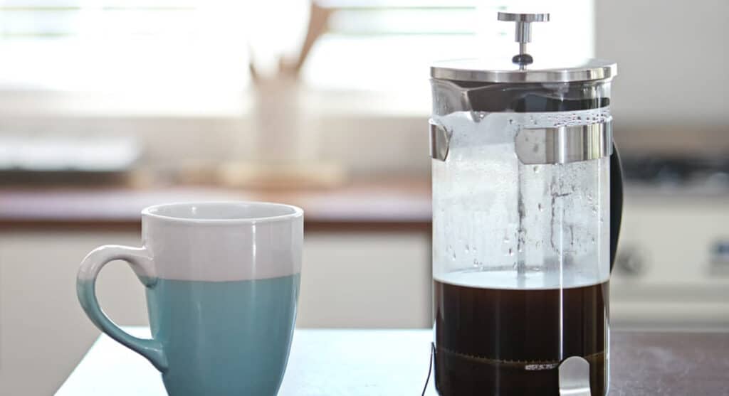 A french press coffee maker next to a cup of coffee.