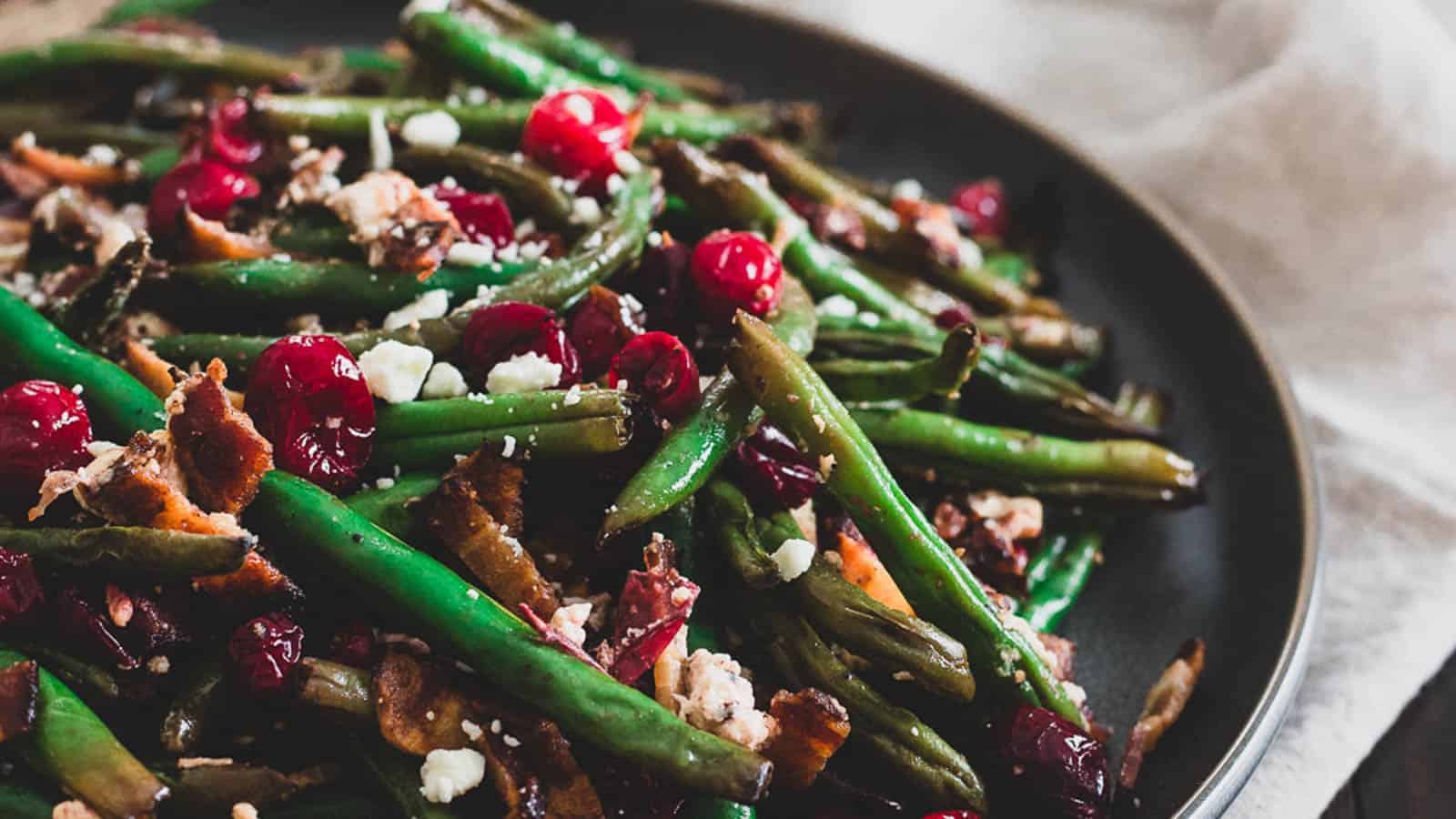 Green beans and cranberries on a plate with bacon and goat cheese.