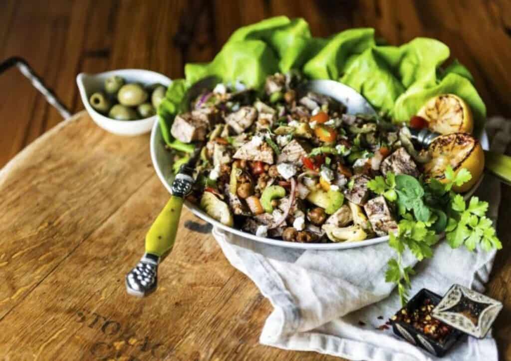 A bowl of salad with diced chicken, lettuce and olives.